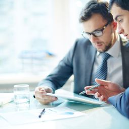 Two men looking at a tablet talking News Article