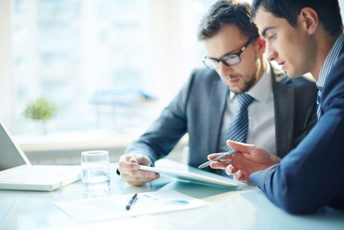 Two men looking at a tablet talking News Article