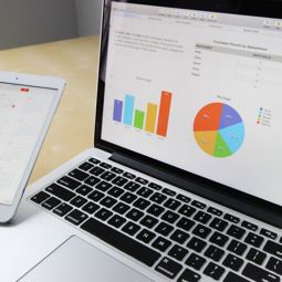 Laptop displaying graphs and someone holding a tablet with a calendar News Article